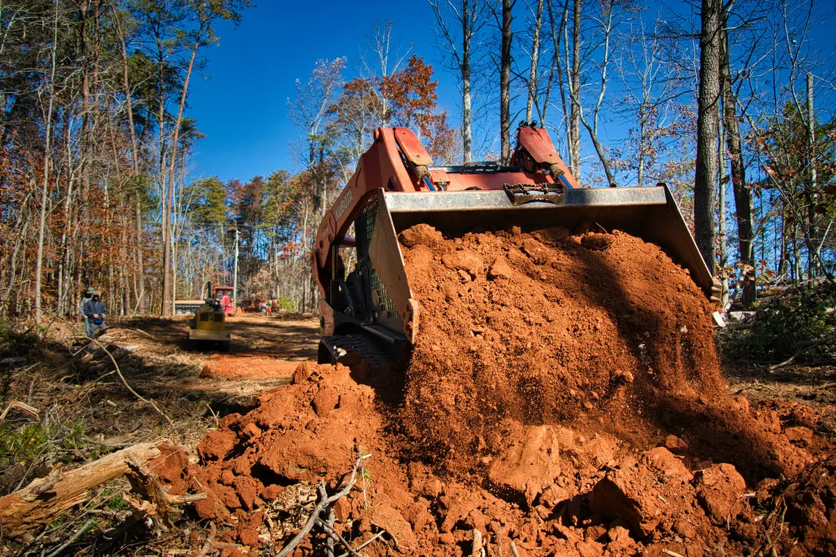 Compact track loader moving material on a wooded site